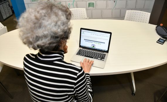 A volunteer older adult is photographed looking at Fountain of Health online.