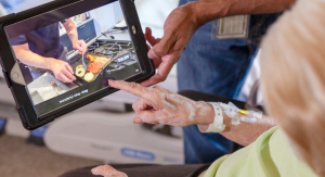 Older woman pointing at a tablet while a video is being played. The video shows food being prepared.