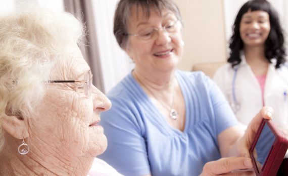 Senior women use smartphone while point-of-care worker looks on