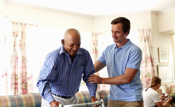 Point-of-care worker assisting a senior man to walk with a walker