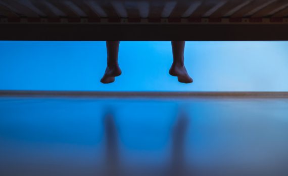 Legs dangling over the end of a bed at night