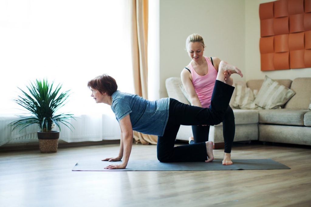 Point-of-care worker helping senior stretch on a yoga mat in a home setting