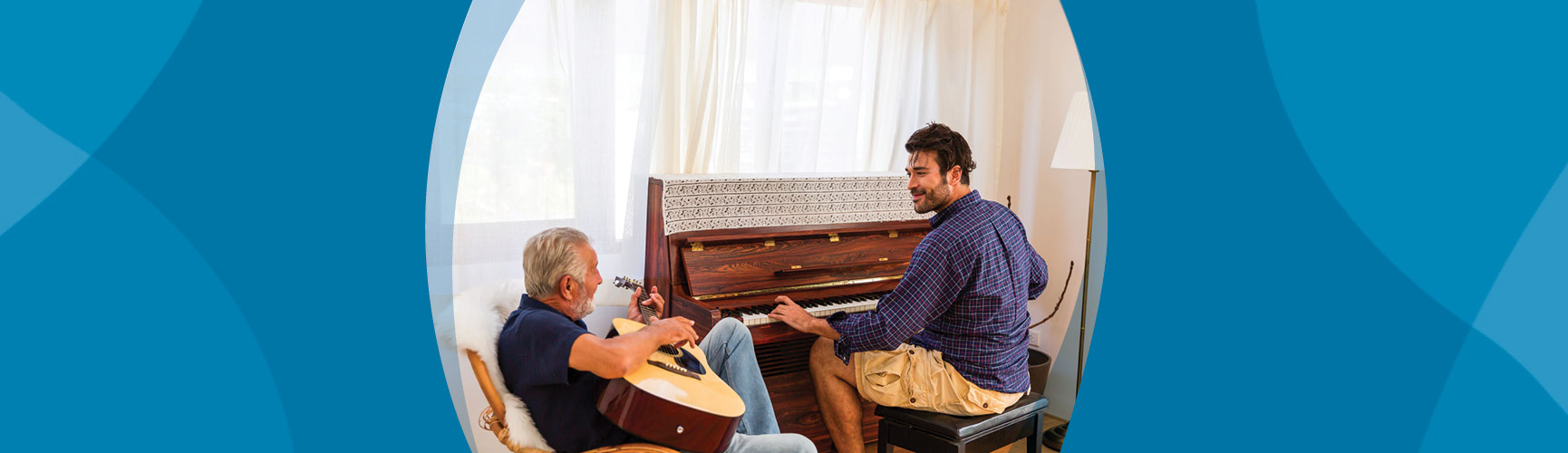 Older man, seated, plays guitar alongside younger man playing piano. Both look happy.