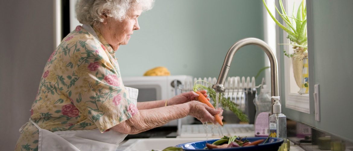 Older adult woman washing vegetables at her kitchen sink.