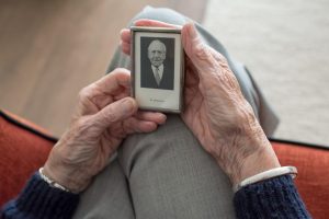 An elderly pair of hands holds a "In memoriam" photo of a loved one.