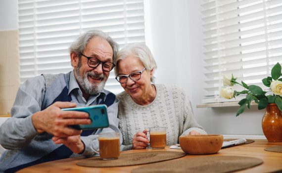 An older man and woman smiling into a phone