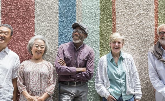 A group of diverse seniors stand up against a multi-coloured wall